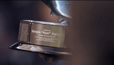 A Person Holding A Trophy That Says Sergio " Kun " On It GIF