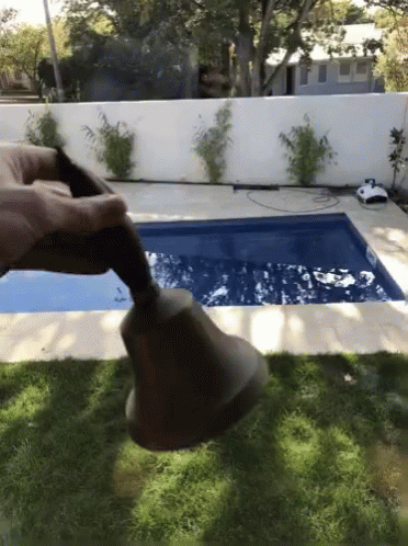 A Person Holds A Bell In Front Of A Pool GIF