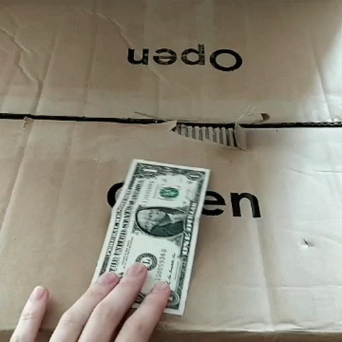A Person Holds A Dollar Bill In Front Of A Cardboard Box That Says Open GIF