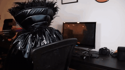 A Person In A Black Costume Sits In Front Of A Computer Monitor GIF