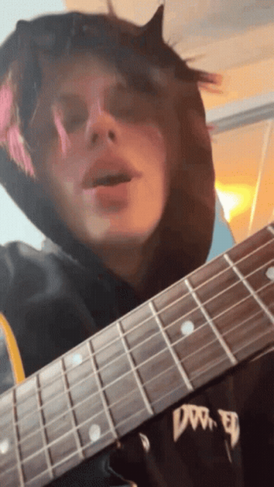 A Person In A Black Hoodie Is Playing A Guitar With The Word Dw On The Neck GIF