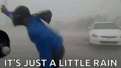 A Person In A Blue Shirt Is Standing In Front Of A Car In The Rain . GIF