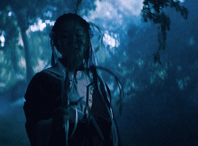 A Person In A Dark Forest Holding A Feather In Their Hand GIF