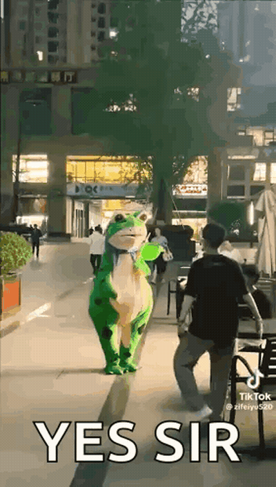 A Person In A Frog Costume Is Walking Down A Street . GIF
