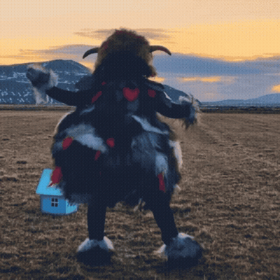A Person In A Furry Costume Stands In A Field With A Small Blue House In The Background GIF