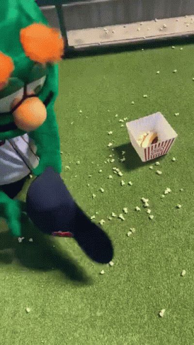 A Person In A Green Costume Is Kicking A Popcorn Bucket On The Grass . GIF