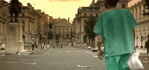A Person In A Green Scrub Is Walking Down An Empty City Street . GIF