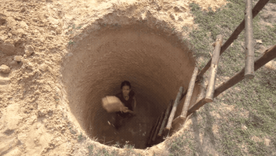A Person In A Hole With A Wooden Ladder Leading To It GIF