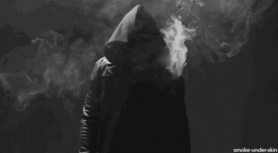 A Person In A Hooded Jacket Is Smoking A Cigarette In A Dark Room GIF