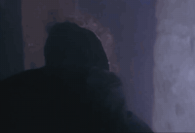A Person In A Hooded Jacket Is Standing In The Dark . GIF