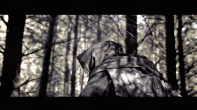 A Person In A Hooded Jacket Is Walking Through A Dark Forest GIF