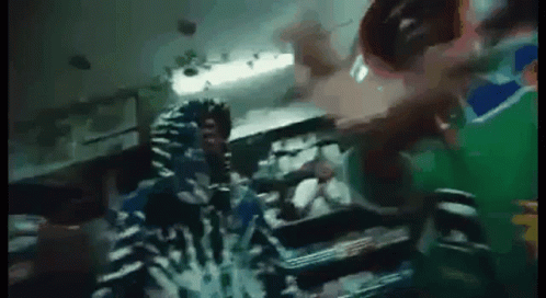 A Person In A Hoodie Is Standing In A Dark Room With A Green Background . GIF