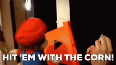 A Person In A Mario Costume Is Holding An Orange Bucket And Says Hit ' Em With The Corn . GIF