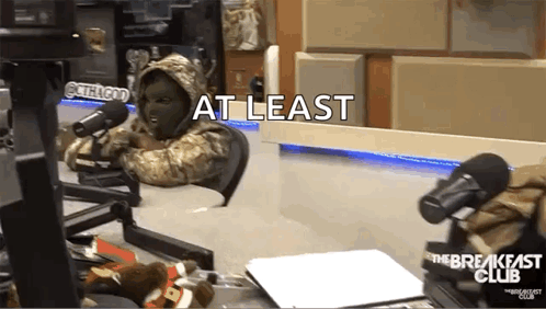 A Person In A Mask Is Sitting In Front Of A Microphone With The Words At Least Written On The Bottom GIF