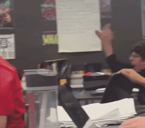 A Person In A Red Shirt Is Raising Their Hand In A Classroom GIF