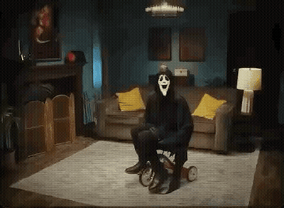 A Person In A Scary Mask Is Sitting On A Tricycle In A Living Room . GIF