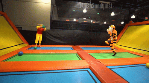 A Person In A Tigger Costume Is Jumping On A Trampoline With Another Person In A Clown Costume GIF