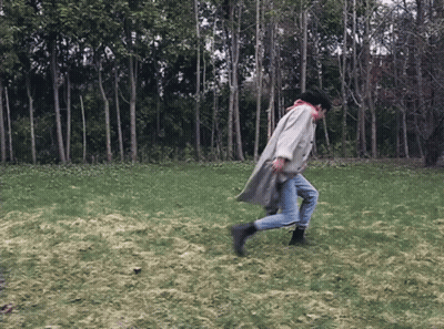 A Person In A Trench Coat Is Running In A Field GIF