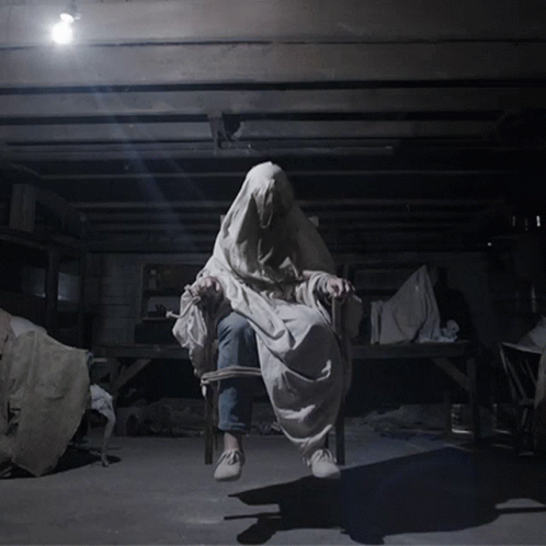 A Person In A White Cloth Is Sitting In A Chair In A Dark Room GIF