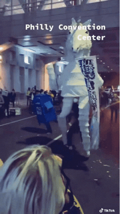 A Person In A White Seahorse Costume Is Walking Down The Street In Front Of The Philly Convention Center GIF