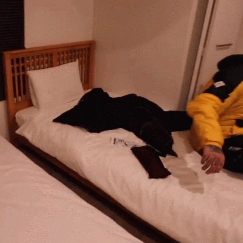 A Person In A Yellow Jacket Is Laying On A Bed With A Book On It GIF