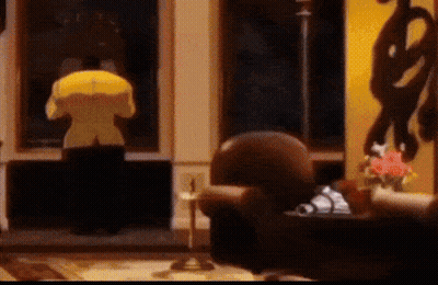 A Person In A Yellow Jacket Stands In A Living Room GIF