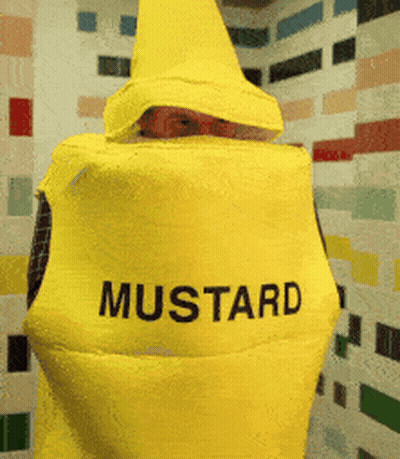 A Person In A Yellow Mustard Costume Is Standing In Front Of A Tiled Wall GIF