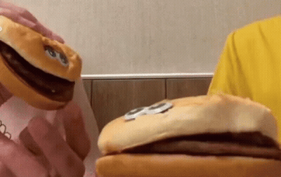 A Person In A Yellow Shirt Is Holding A Stuffed Hamburger With A Face On It GIF