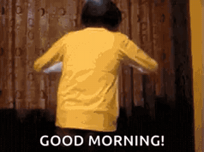 A Person In A Yellow Shirt Is Standing In Front Of A Curtain And Says `` Good Morning '' . GIF