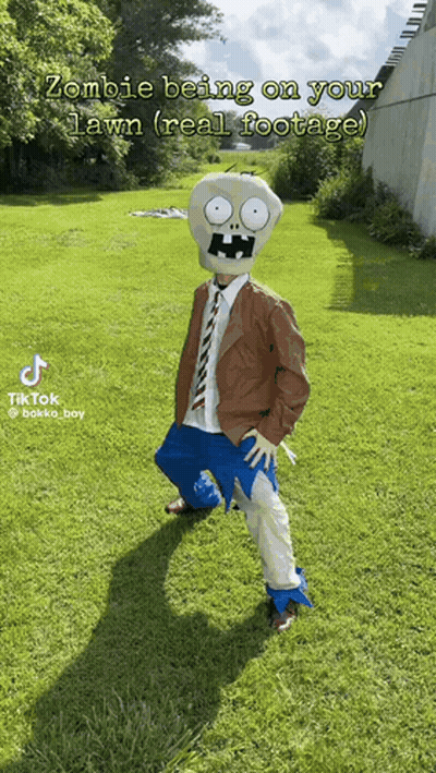 A Person In A Zombie Costume Is Standing On A Lush Green Lawn GIF