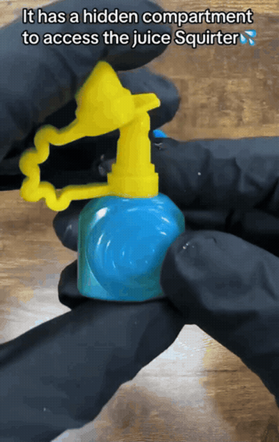 A Person In Black Gloves Is Holding A Juice Squirter That Has A Hidden Compartment To Access The Juice GIF