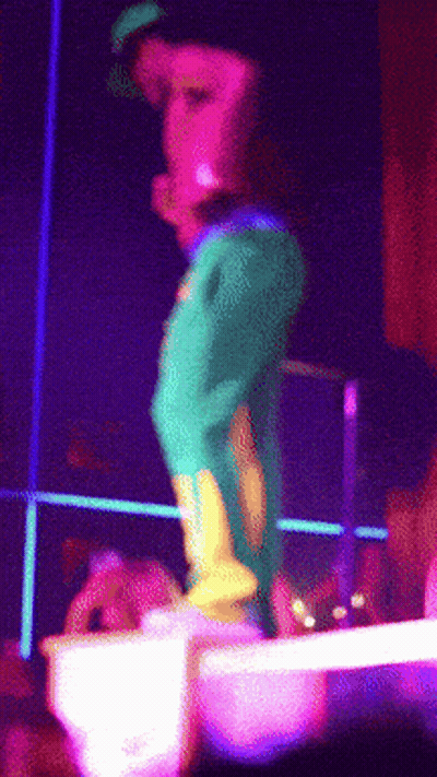A Person In Green Pants And Yellow Boots Is Standing On A Stage GIF
