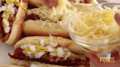 A Person Is Adding Cheese To A Hot Dog Sandwich . GIF