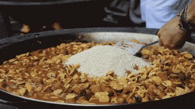 A Person Is Adding Rice To A Large Pot Of Food GIF