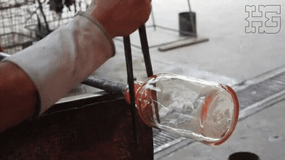 A Person Is Blowing A Glass Bottle With Tongs In A Factory GIF