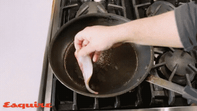 A Person Is Cooking Bacon In A Frying Pan With Esquire Written On The Stove Top GIF