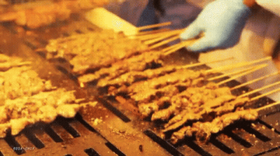 A Person Is Cooking Meat On Skewers On A Grill GIF