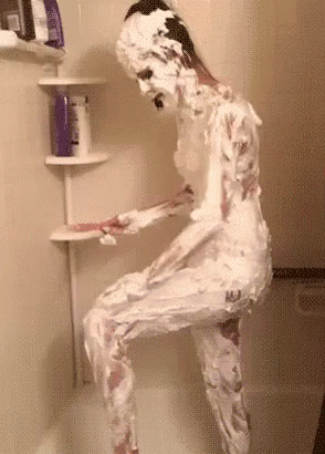 A Person Is Covered In Shaving Cream In A Shower Stall . GIF