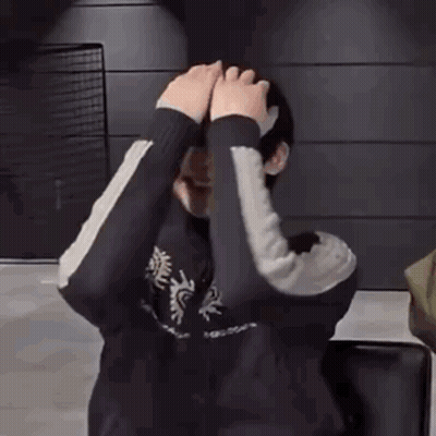 A Person Is Covering Their Face With Their Hands While Standing In Front Of A Wall . GIF