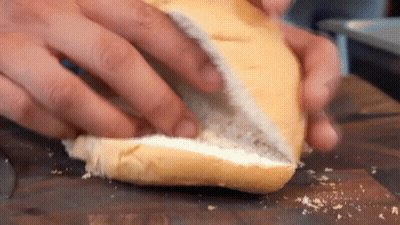 A Person Is Cutting A Bun In Half On A Cutting Board . GIF