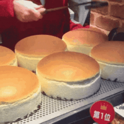 A Person Is Cutting A Cheesecake With A Knife In A Bakery . GIF