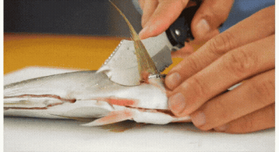 A Person Is Cutting A Fish With A Knife On A Table GIF