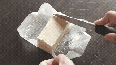 A Person Is Cutting A Piece Of Butter With A Knife On A Table GIF