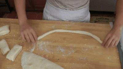 A Person Is Cutting A Piece Of Dough On A Wooden Table With An Apple Pie Box In The Background GIF