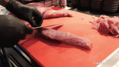 A Person Is Cutting A Piece Of Meat On A Red Cutting Board That Says Made In Animotica GIF