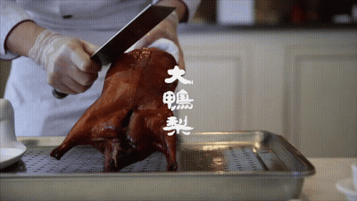 A Person Is Cutting A Roasted Duck With Chinese Writing On The Bottom GIF