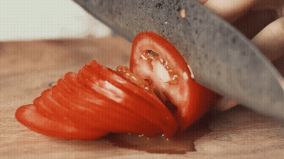 A Person Is Cutting A Tomato In Half On A Cutting Board GIF