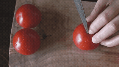 A Person Is Cutting A Tomato With A Knife On A Cutting Board GIF