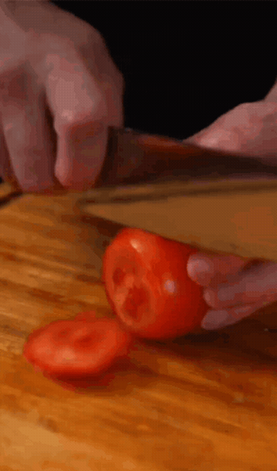 A Person Is Cutting A Tomato With A Knife On A Wooden Cutting Board GIF