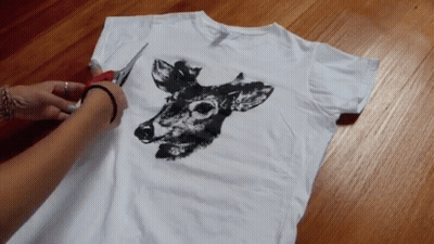 A Person Is Cutting A White T-Shirt With A Deer On It GIF